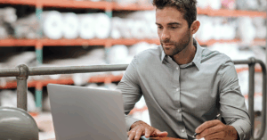 a man in a warehouse typing on a laptop